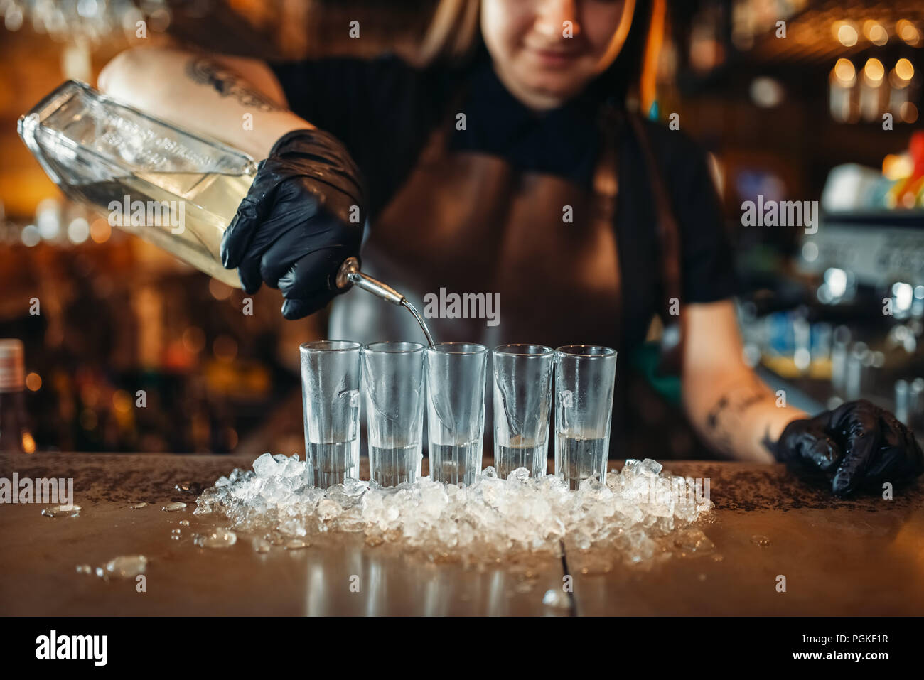 Female barman in gloves puts drinks on ice. Woman bartender mixing at the bar counter in pub. Barkeeper occupation Stock Photo