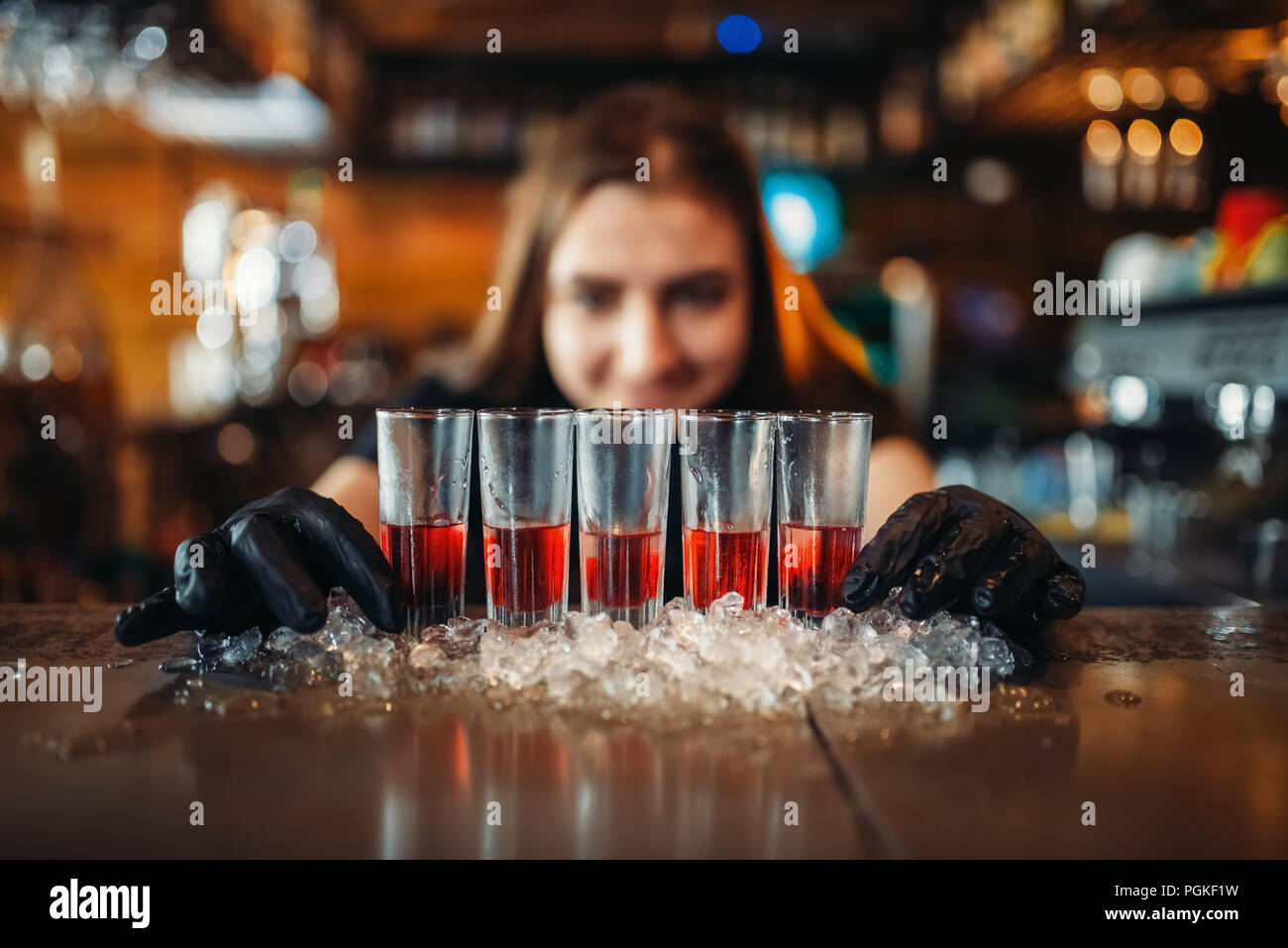 Female barman in gloves puts drinks on ice. Woman bartender mixing at the bar counter in pub. Barkeeper occupation Stock Photo