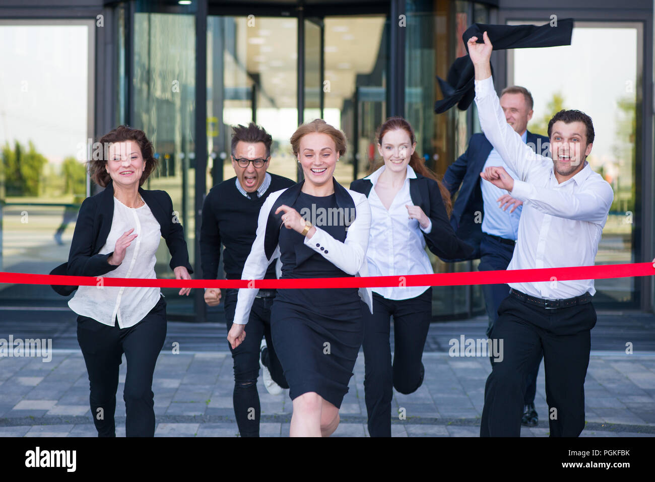 Group of happy business people running from office building crossing red ribbon finish line Stock Photo