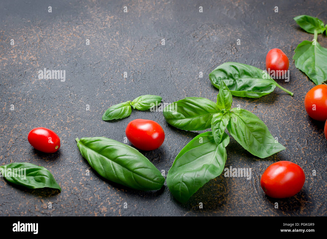 a lot of scattered green fresh basil leaves and cherry tomatoes on a dark rusty old background, close up  Top view, copy space Stock Photo