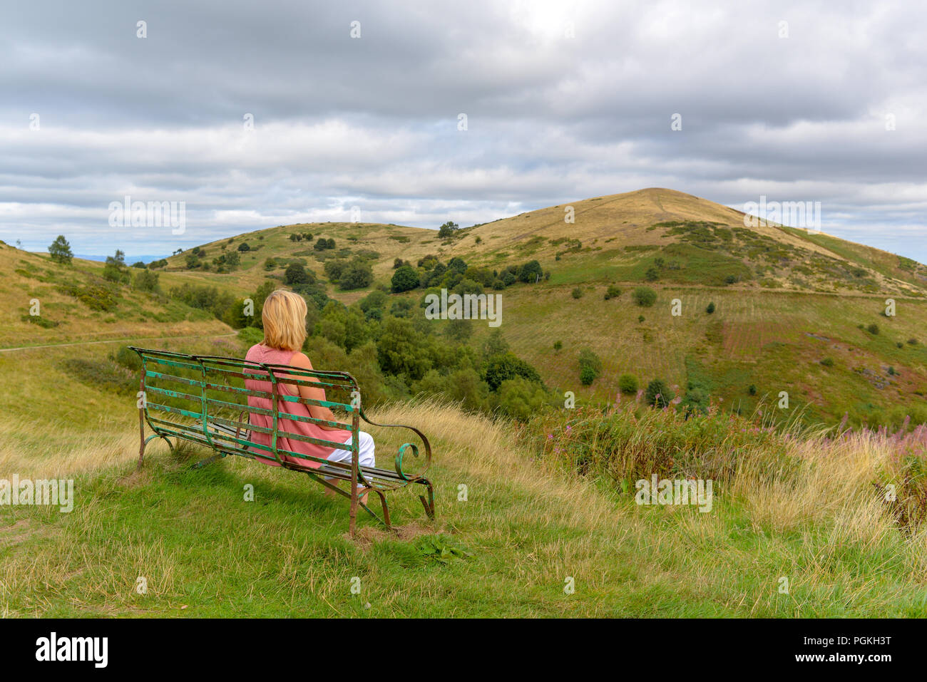 Woman sitting on a bench overlooking North Hill, Malvern Hills, Worcestershire, England, UK Stock Photo