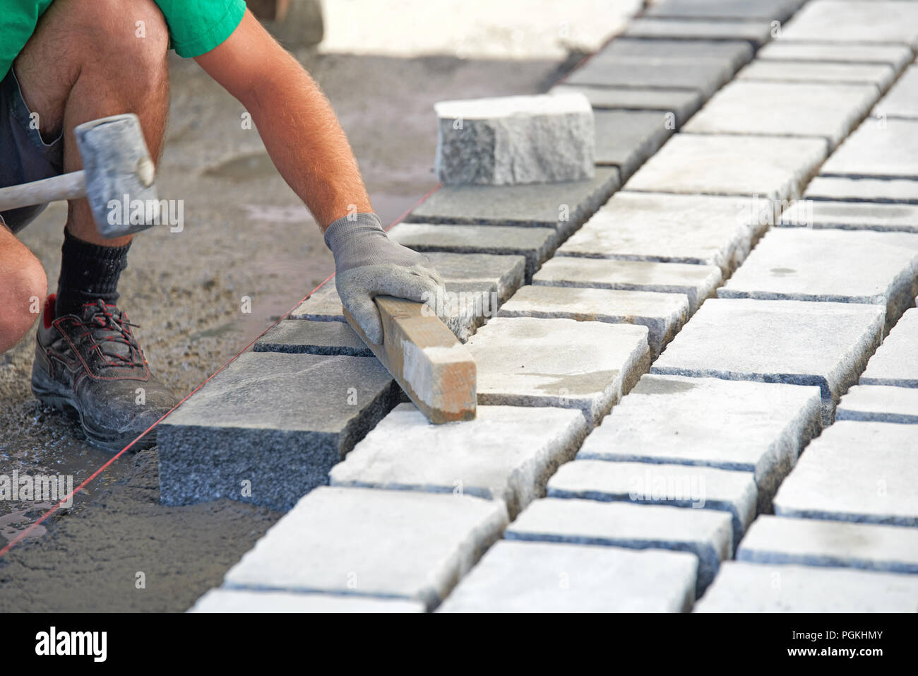A workman's gloved hands use a hammer to place stone pavers. Worker