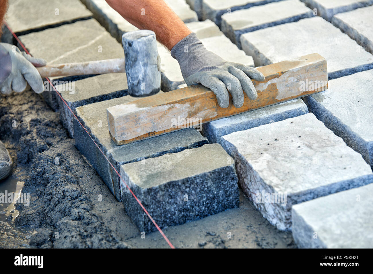 A workman's gloved hands use a hammer to place stone pavers. Worker