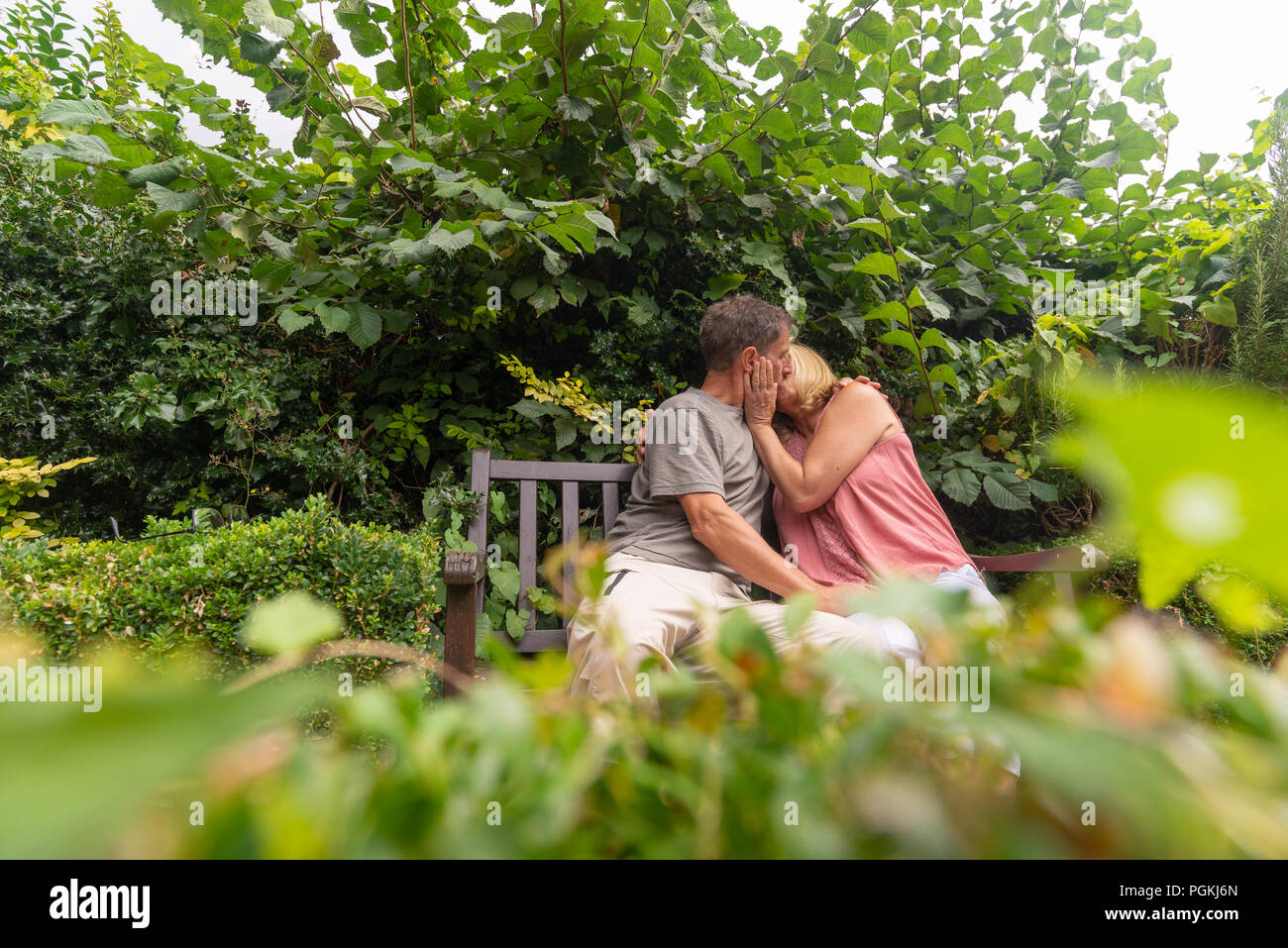 Couple sitting on a bench in a park in an embrace and kissing. Stock Photo