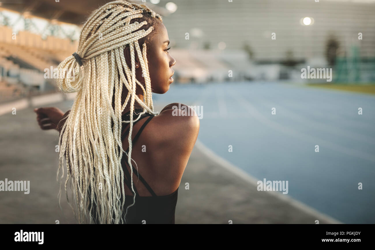 Side view of a woman athlete doing stretching exercises in a track and field stadium. Athlete warming up before a run stretching her hands inside a st Stock Photo