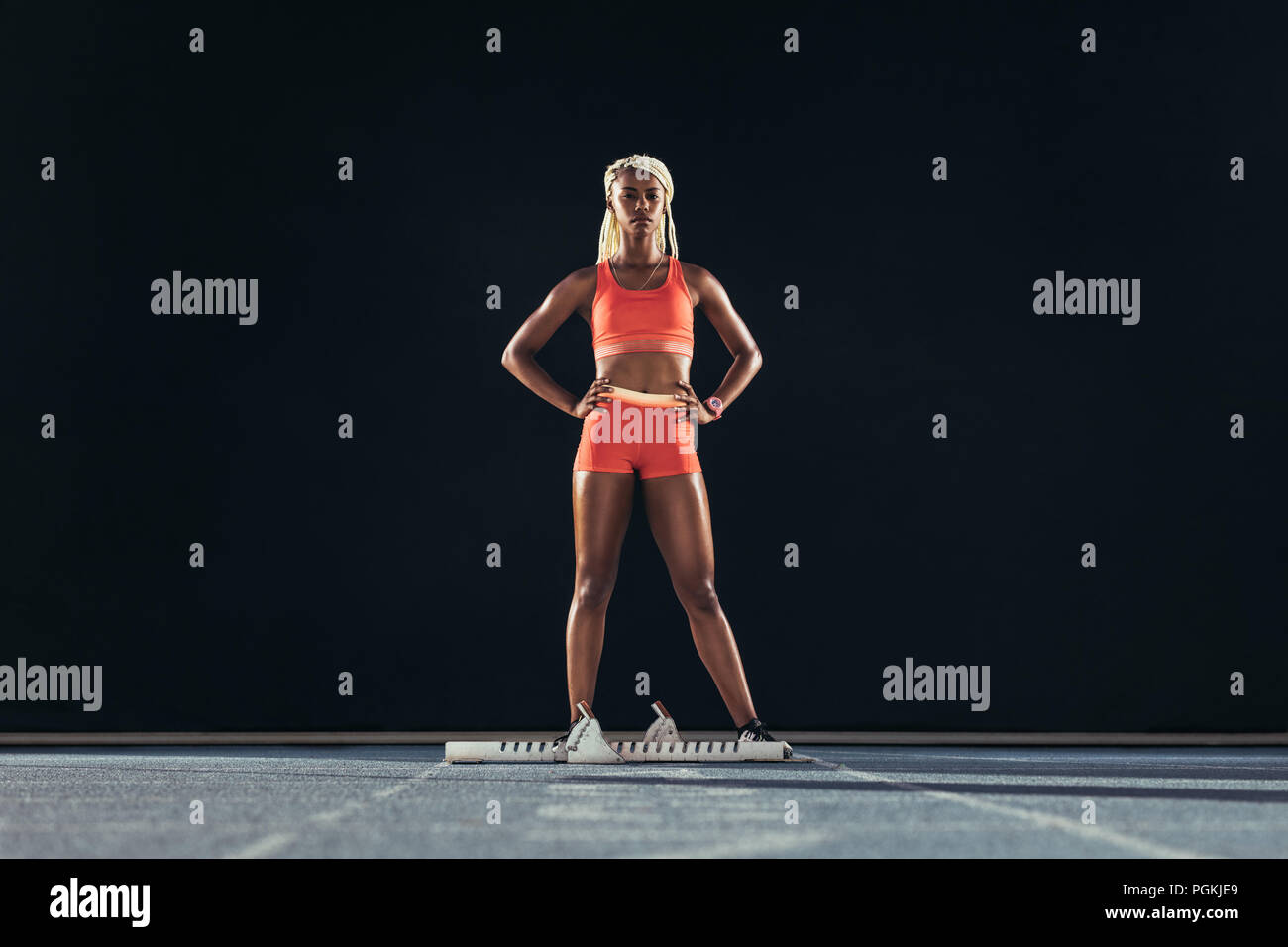 Female sprinter standing beside a starting block on running track on a ...