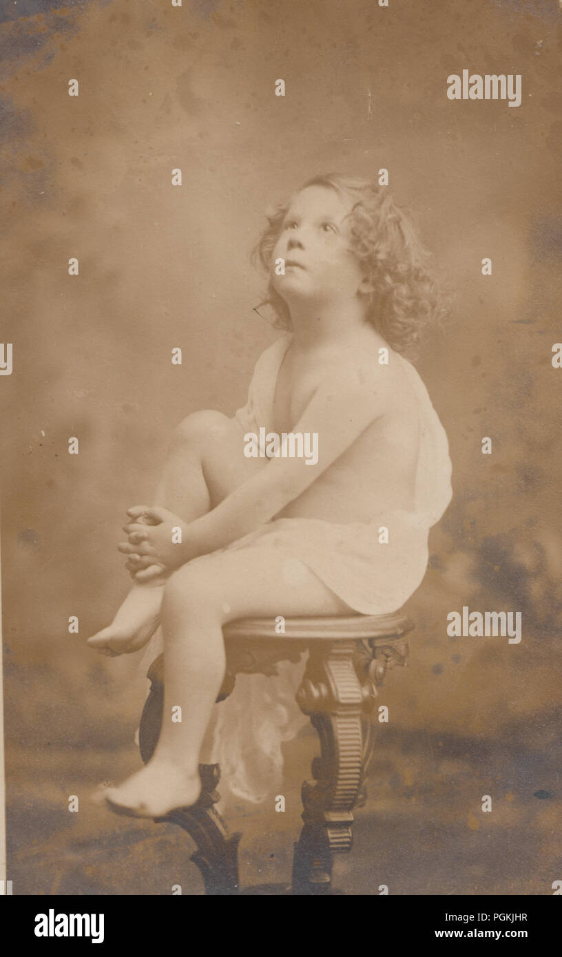 Vintage Photograph of a Blond Curly Haired Boy Child Sat on a Pedestal Wearing a Toga (Cherub Image) Stock Photo