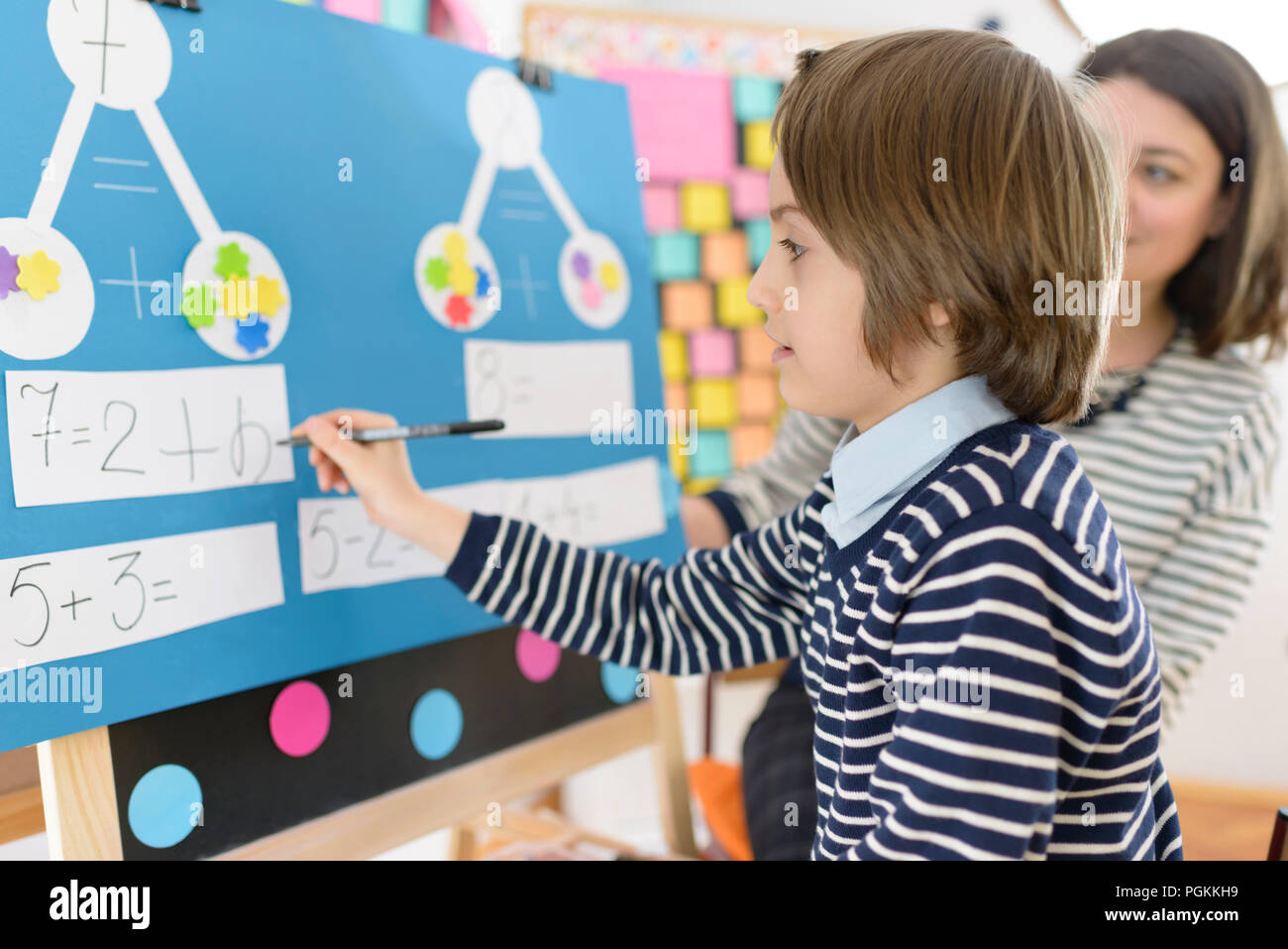 Cute boy solving graphic math exercises at kindergarten, under educator observation Stock Photo