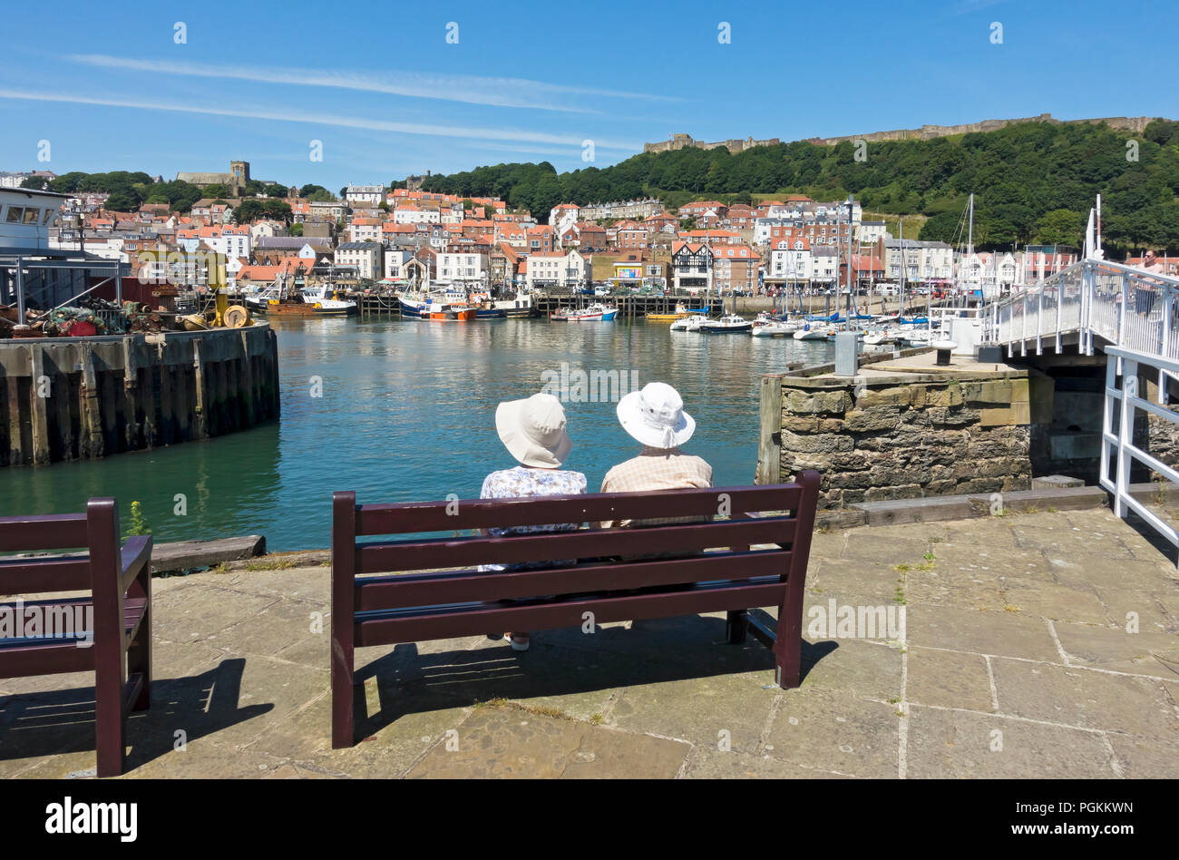 Senior people tourists visitors sitting sat on bench on harbour wall in summer Scarborough North Yorkshire England UK United Kingdom GB Great Britain Stock Photo