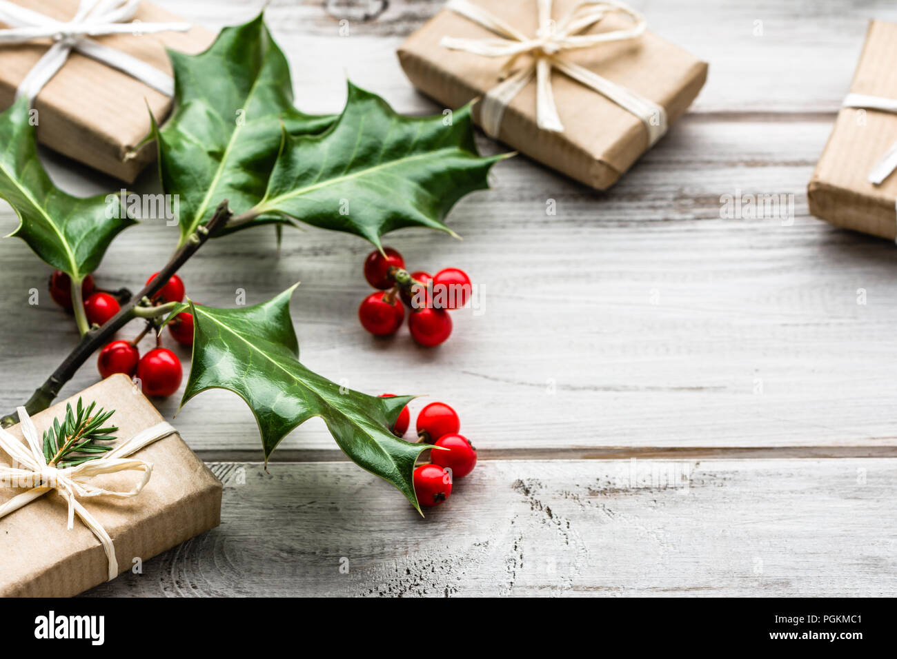 Christmas gift box, present in rustic package decorated with green fir branch and holly plant on white background Stock Photo