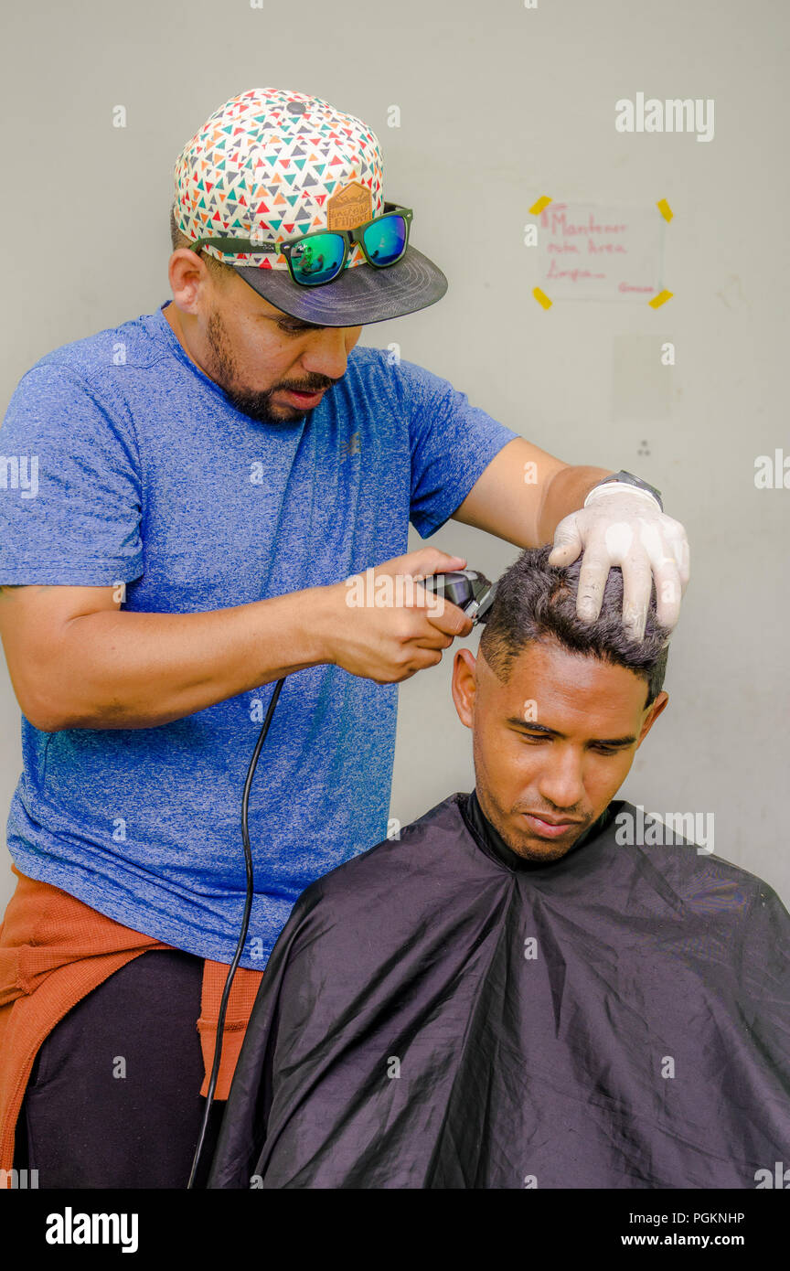 QUITO, ECUADOR, AUGUST 21, 2018: Outdoor view of unidentified man wearing gloves and hat, using a cut hair machine in a youg guy, inside of a refuge f Stock Photo