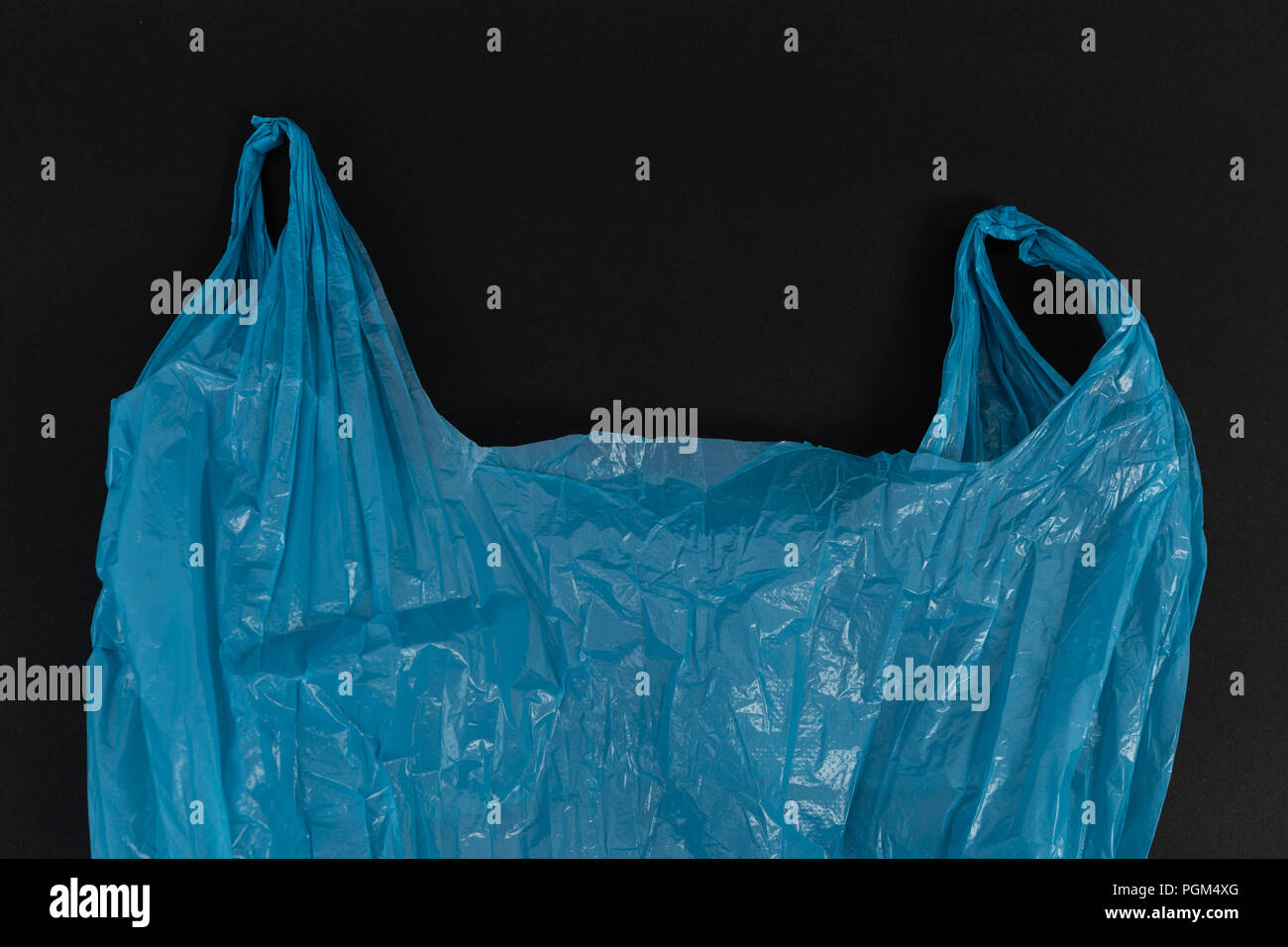 Used crumpled single use blue plastic bag with handles as waste pollution environment ecology concept isolated on black background Stock Photo