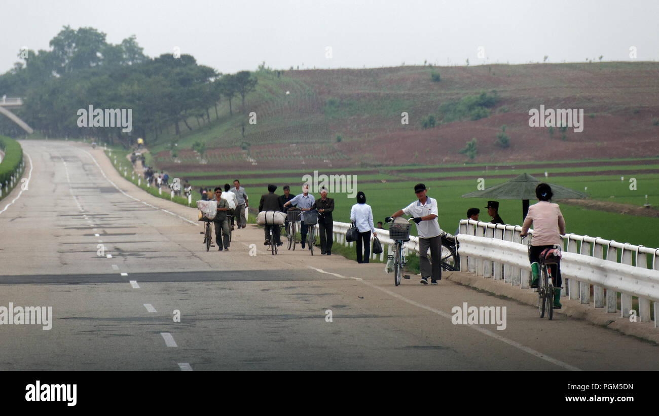 Workers walk or push bicycles along a traffic free empty highway near Pyongyang, North Korea Stock Photo