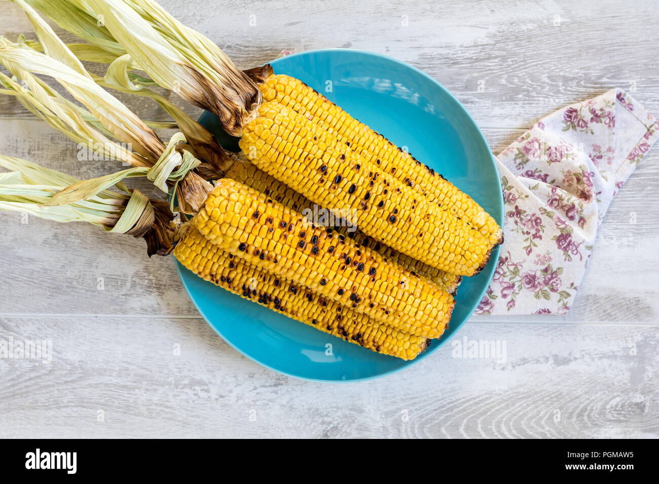 Corn baked in olive oil and salt on blue dish on light surface. Vegetarian, vegan menu Stock