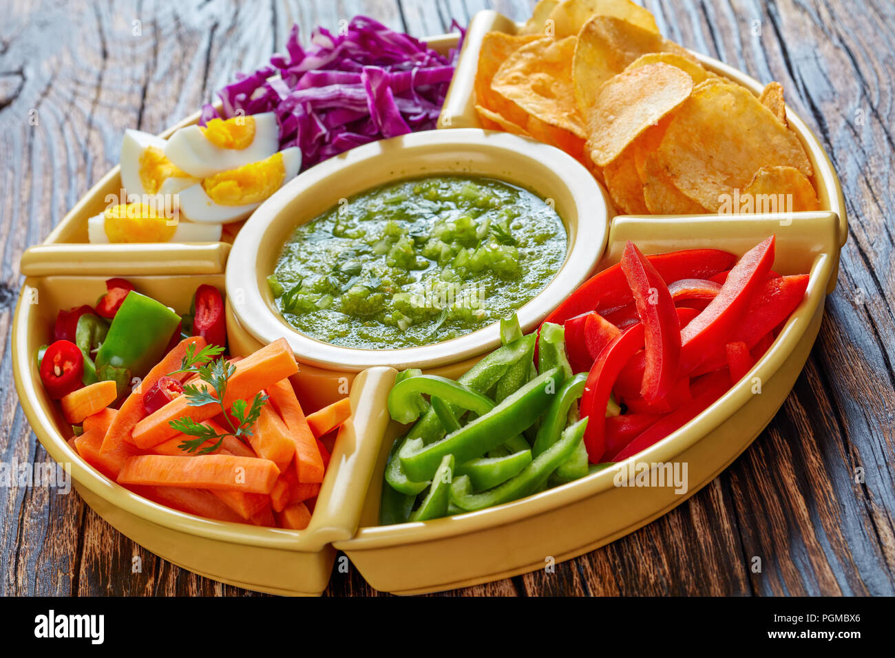 green salsa verde and mexican set of chopped fresh vegetables, hard boiled eggs and chips in bowls on old dark rustic wooden table. ingredients for ta Stock Photo