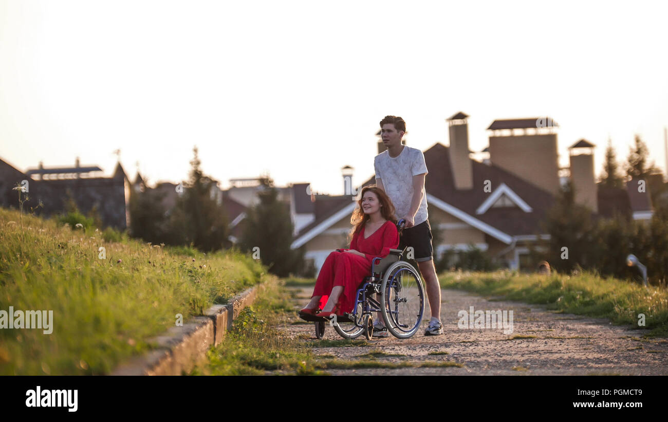A beautiful girl in a wheelchair and her young man are walking in the ...