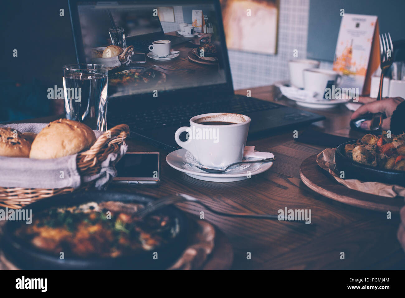 A cup of coffee and breakfast, a laptop computer in a modern cafe bar, a picture of a freelancer. Cozy atmosphere of the designer. Stock Photo