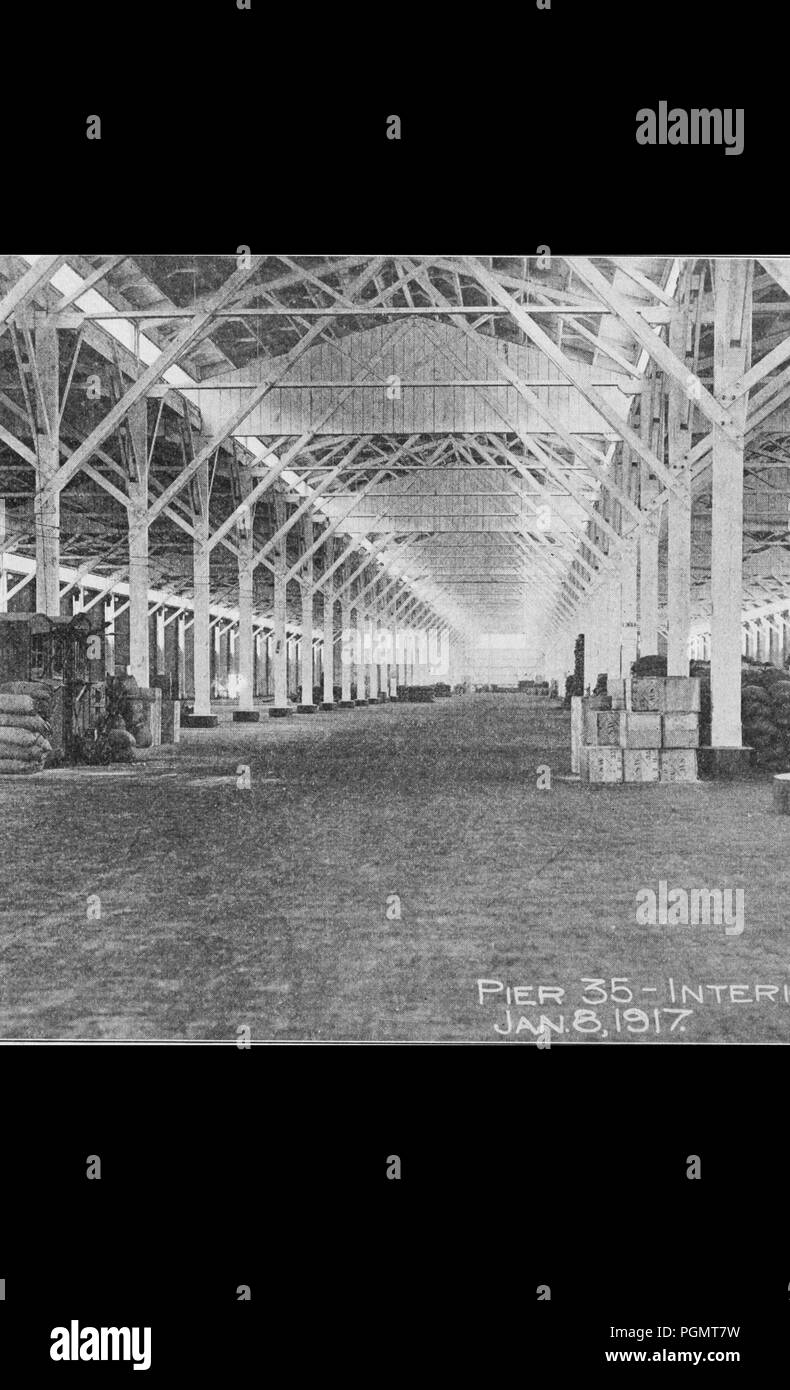 Black and white photograph showing the interior of Pier 35, with a metal roof supported by iron trusswork, and crates and sandbags stacked on either side, located in San Francisco, California, January 8, 1917. Courtesy Internet Archive. () Stock Photo