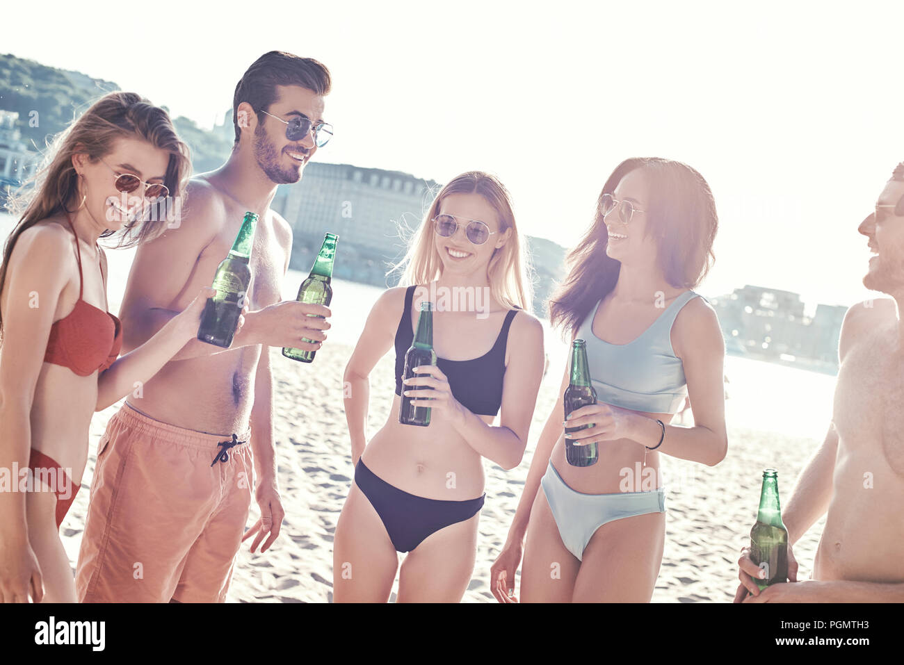 Enjoying carefree time with friends. Cheerful young people spending nice time together while sitting on the beach and drinking beer Stock Photo