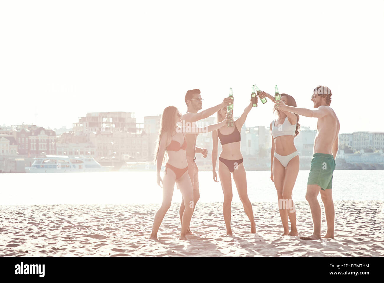 Enjoying carefree time with friends. Cheerful young people spending nice time together while sitting on the beach and drinking beer Stock Photo
