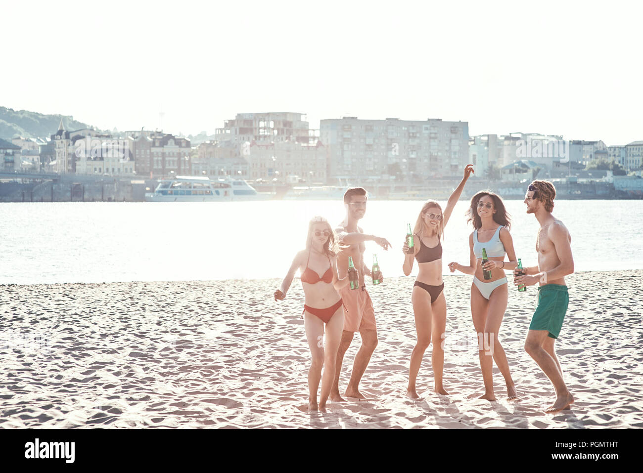 Enjoying carefree time with friends. Cheerful young people spending nice time together while sitting on the beach and drinking beer Stock Photo