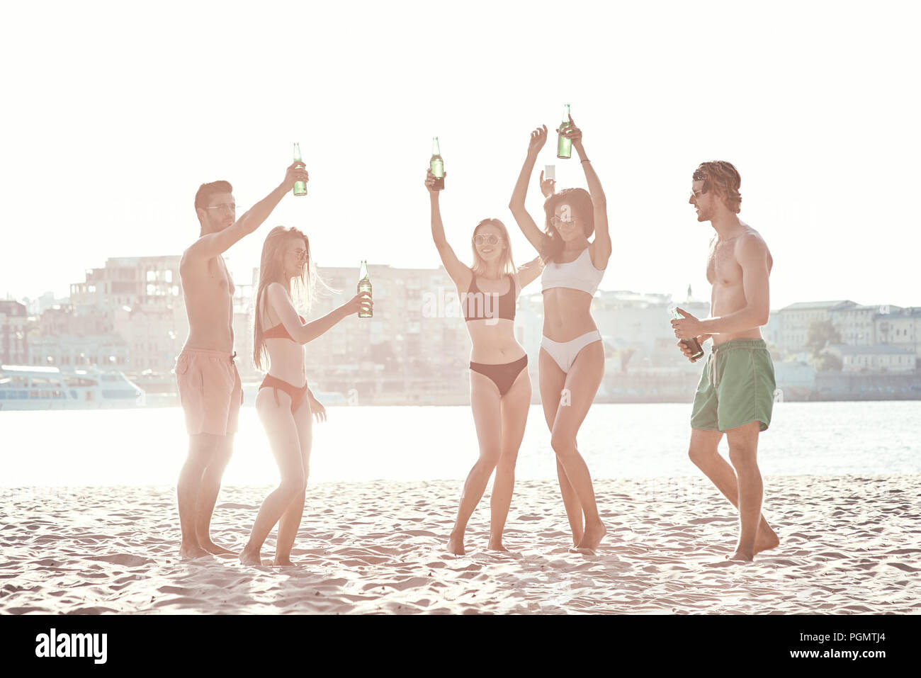 Enjoying carefree time with friends. Cheerful young people spending nice time together while sitting on the beach and drinking beer Stock Photo