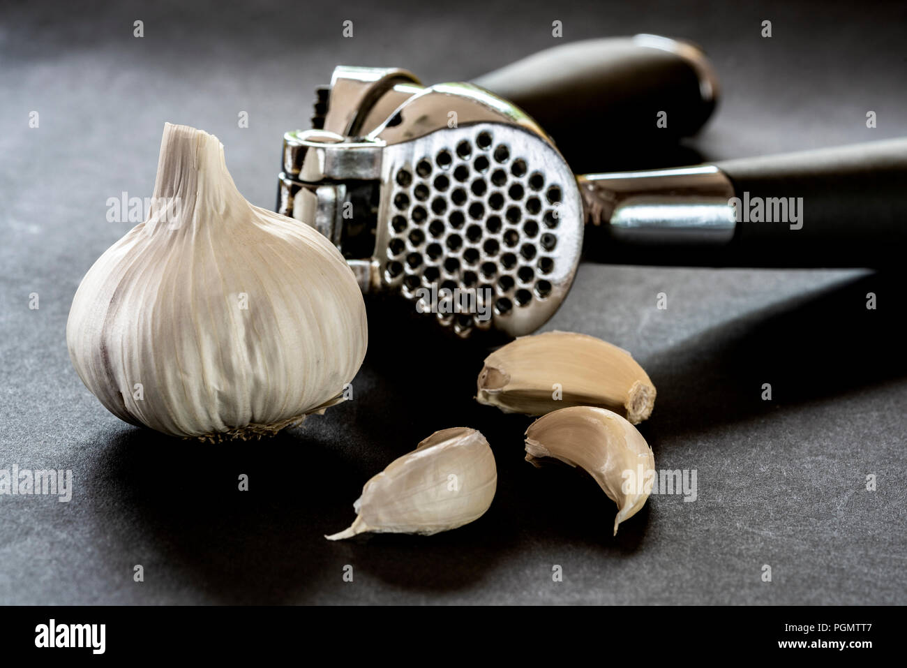 Garlic crusher or press with a bulb and cloves. Stock Photo