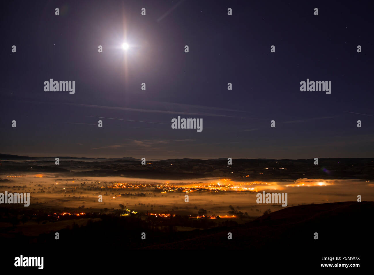 Streetlights of Ruthin at night glowing through fog in the Vale of Clwyd, North Wales, with the moon above Stock Photo
