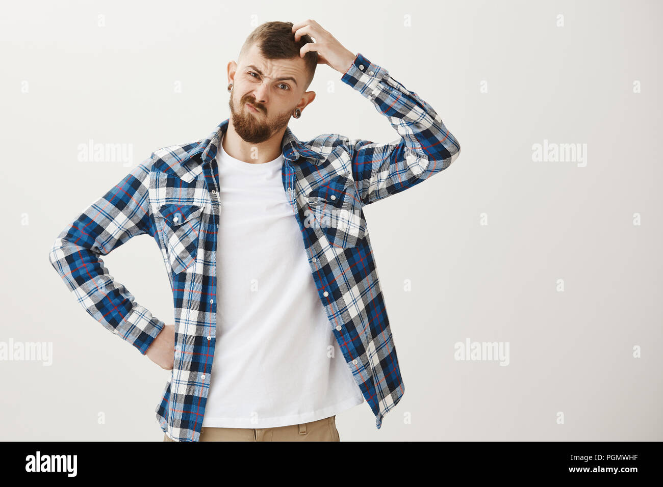 Intense male coworker trying solve issue, being clueless how to find solution. Frowning serious caucasian guy with beard, holding hand on hip and scratching head, trying to understand something Stock Photo