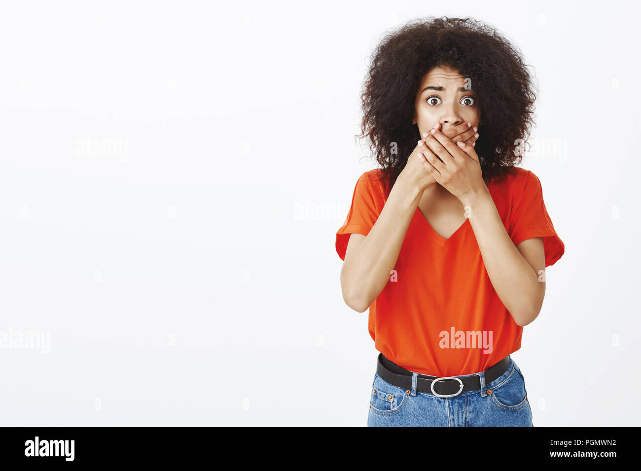 Portrait of shocked worried attractive african-american female sibling with afro haircut, covering mouth with both palms, staring terrified at camera, being speechless from anxiety and shock Stock Photo