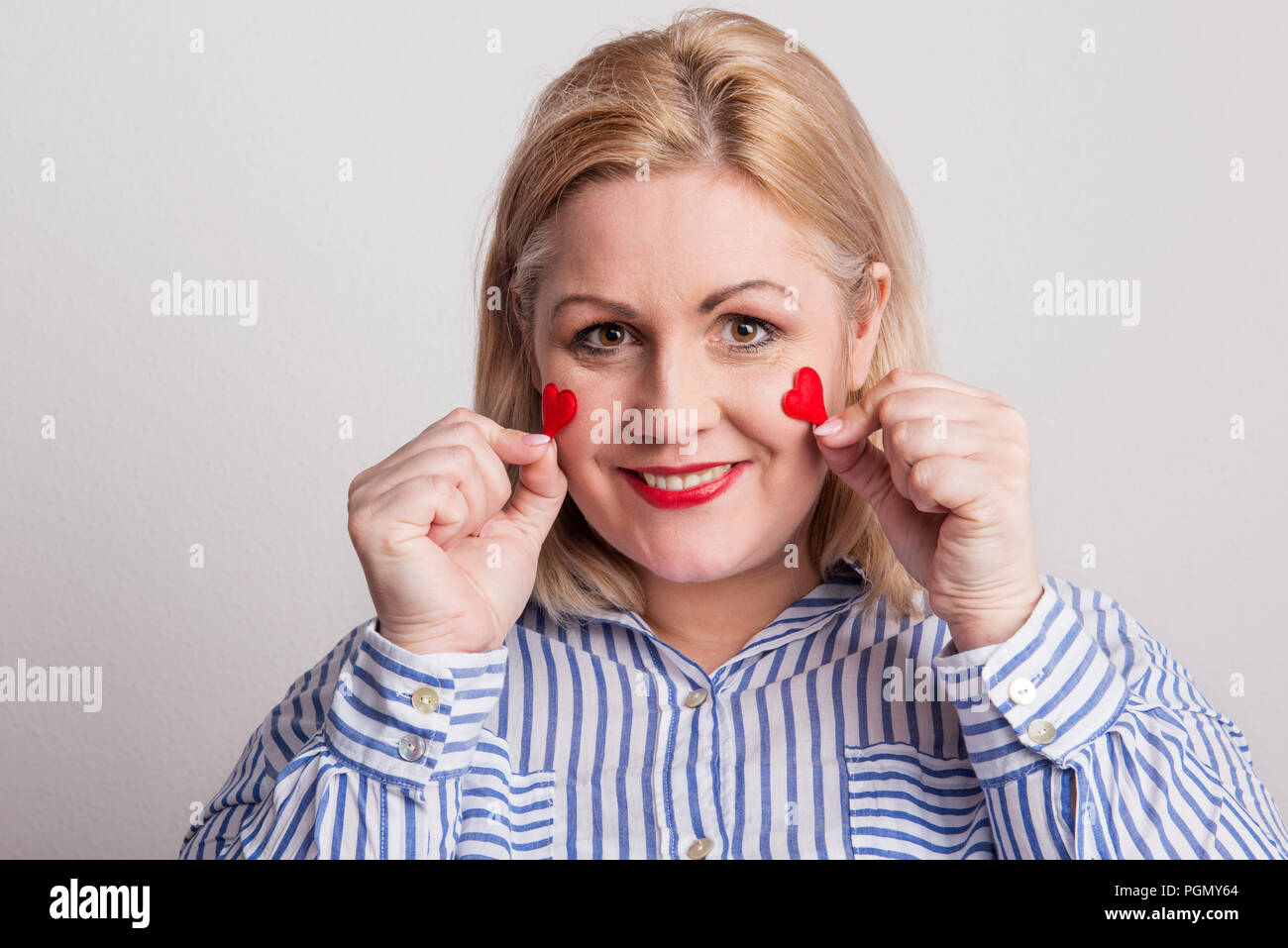 Portrait of an attractive overweight woman holding hearts on her cheeks. Stock Photo