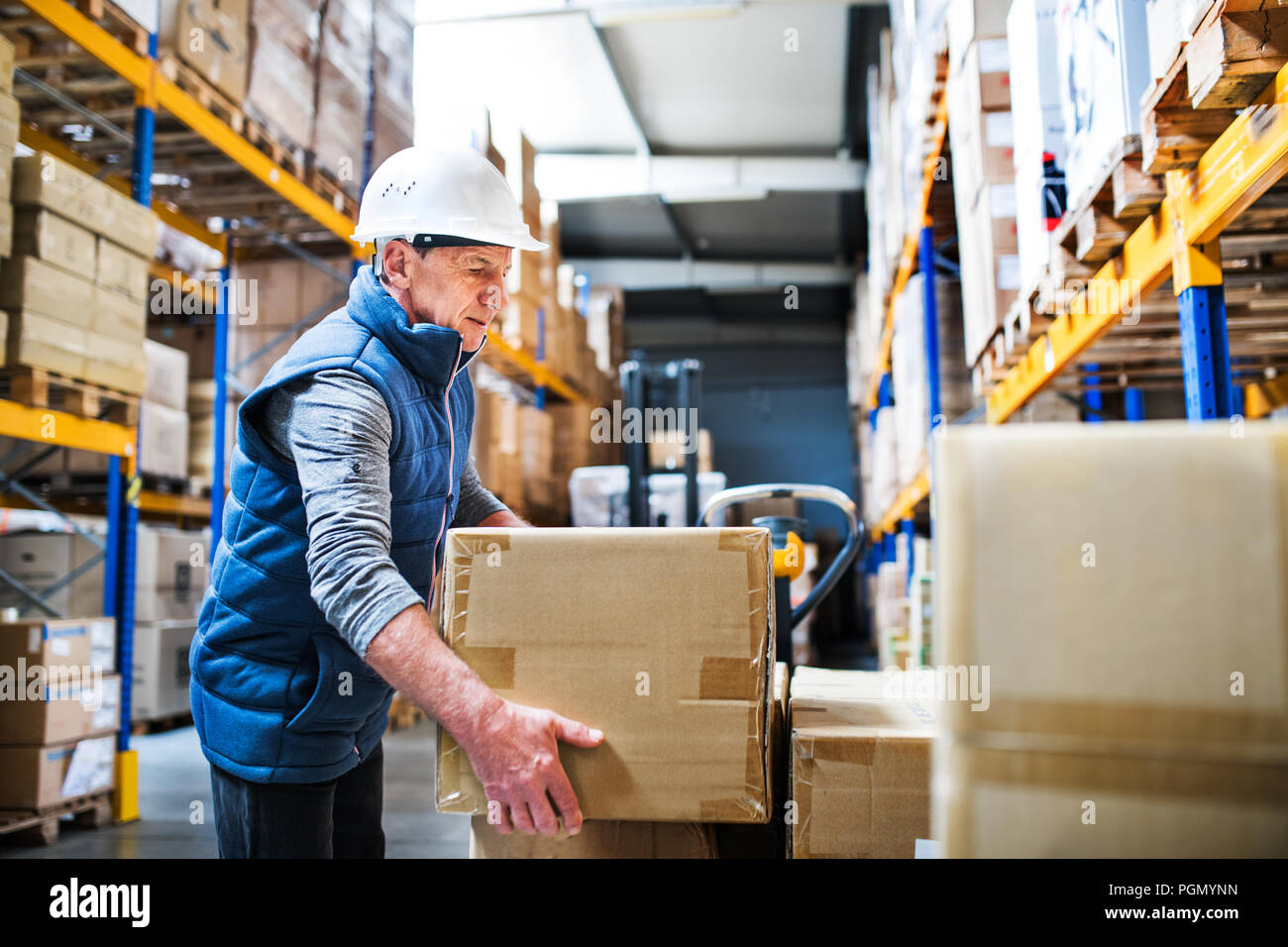 Senior male warehouse worker unloading boxes from a pallet truck Stock