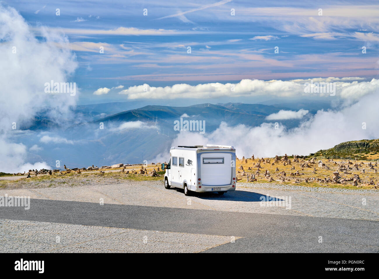 Motor Home parking alone on an asphalt parking lot with view to mountains sunnrounded by thick clouds Stock Photo