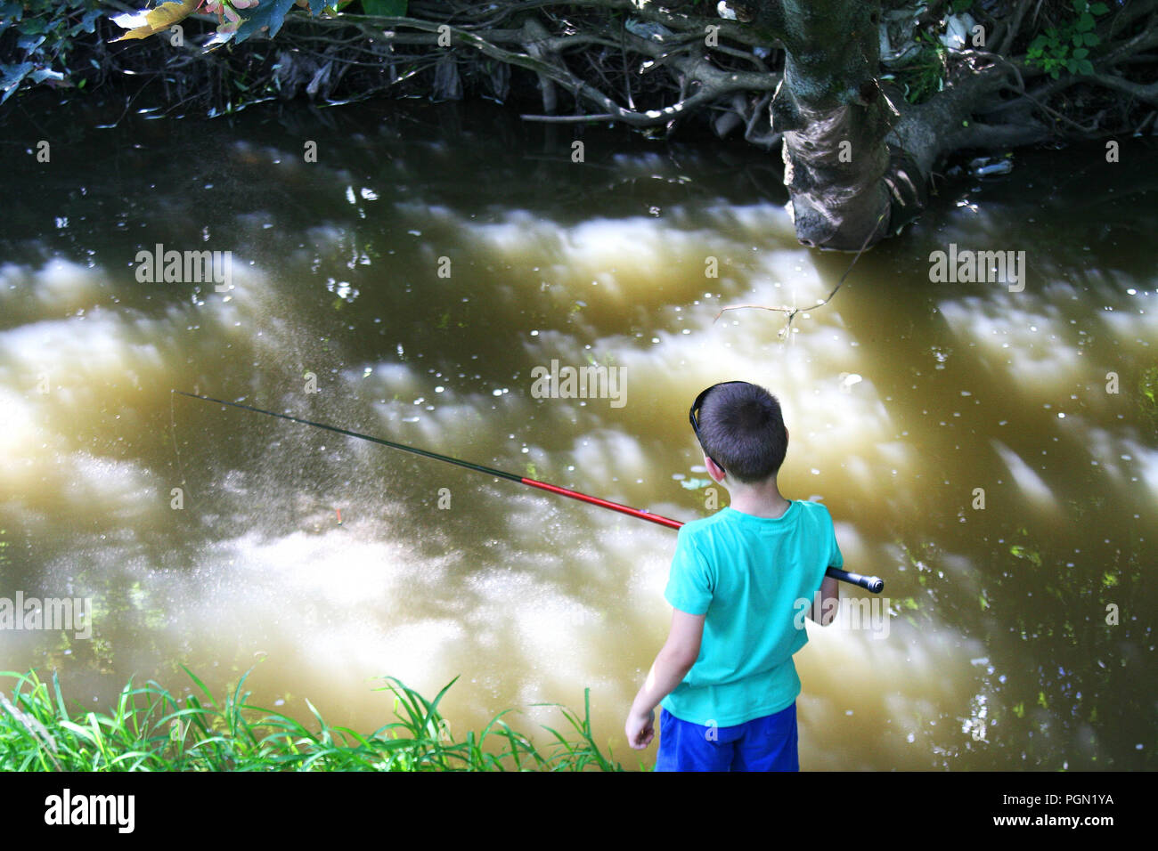 Boy fishing in the shady river. Kid trying to catch fish under the