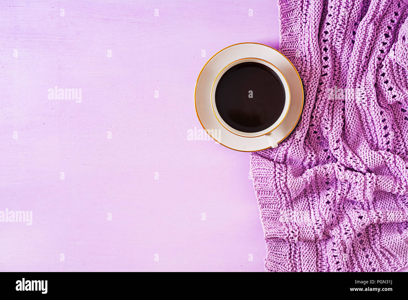 Cup of hot coffee on violet table, close up photo knitted sweater with mug, winter morning concept. Top view. Flat lay Stock Photo