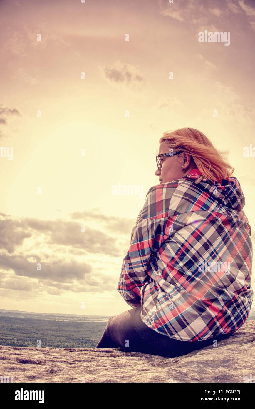 Young girl tourist sits on the edge of the cliff and looks down at the ...