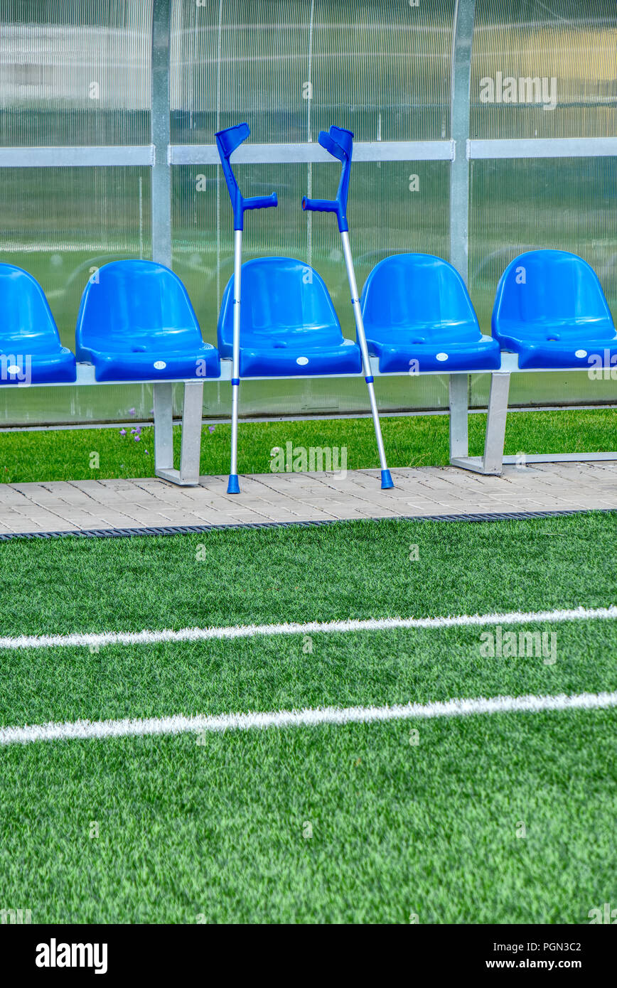 Forearm crutches of hurt player wait at stadium players bench chairs