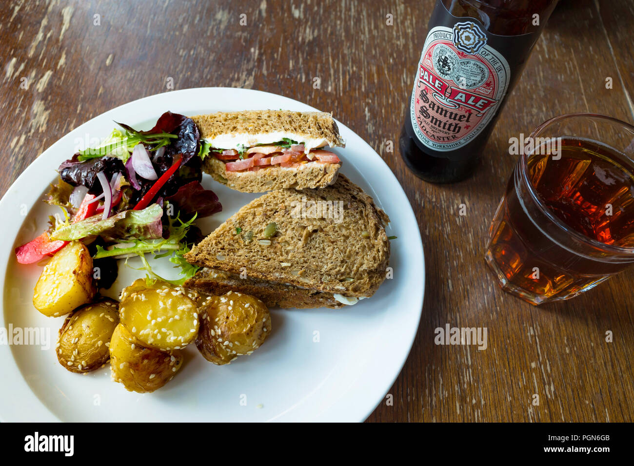 Café lunch a cream cheese and tomato sandwich  on multigrain brown bread with salad sesame potatoes and a glass and bottle of organic Pale Ale Stock Photo