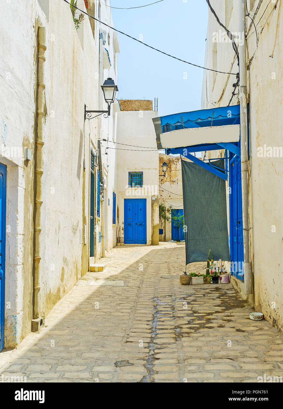 The narrow empty street of medieval Medina, the traditional white houses with bright blue doors and outer clay sewer pipes, Sousse, Tunisia. Stock Photo