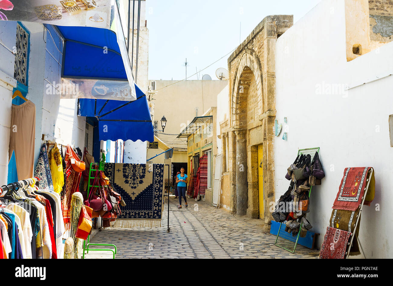 SOUSSE, TUNISIA - AUGUST 28, 2015: The clothes and rug stores around the medieval gateway of Zaouia Zakkar mosque in Medina, on August 28 in Sousse. Stock Photo