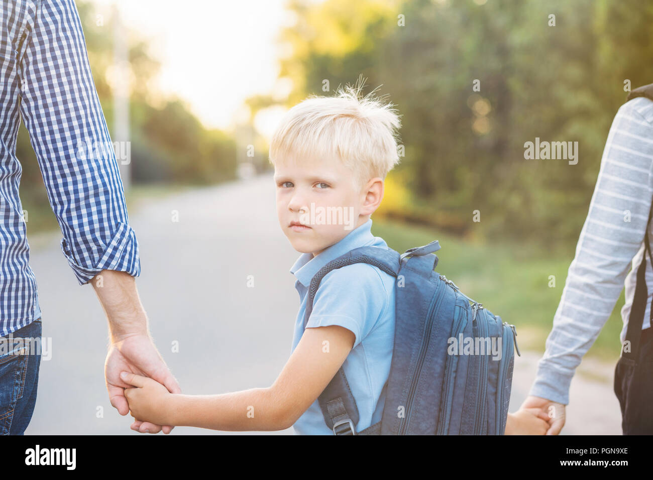 Father and older brother holding little son's hands. Little schoolboy with backpack going to school. Back to school concept. Stock Photo