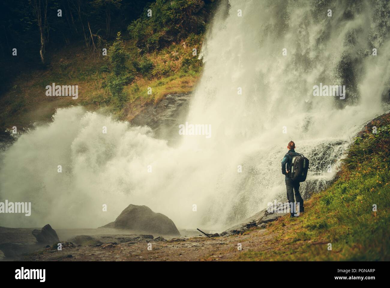 Caucasian Hiker and the Scenic Waterfall. Men with Backpack Exploring the Nature. Stock Photo