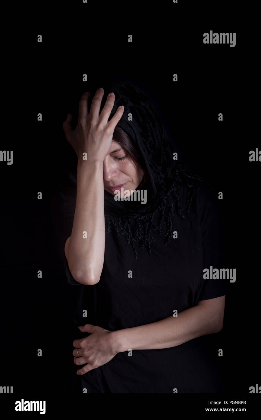 Beautiful woman in black head scarf depressed (black background) Stock Photo