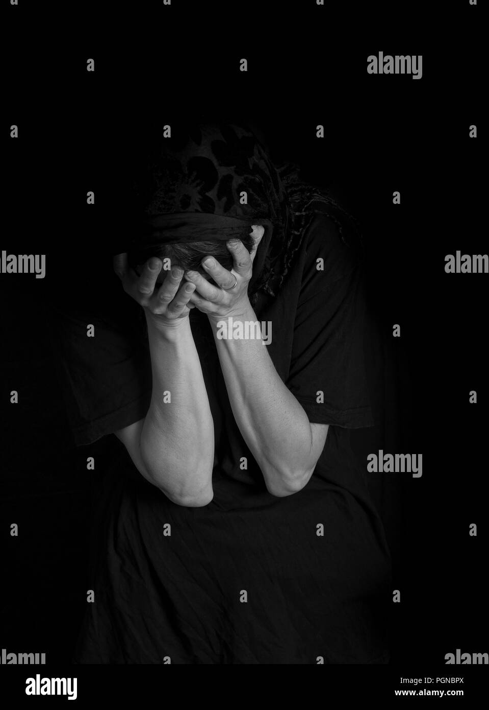 Woman sitting with her hands covering her face - concept of sorrow (monochrome image) Stock Photo