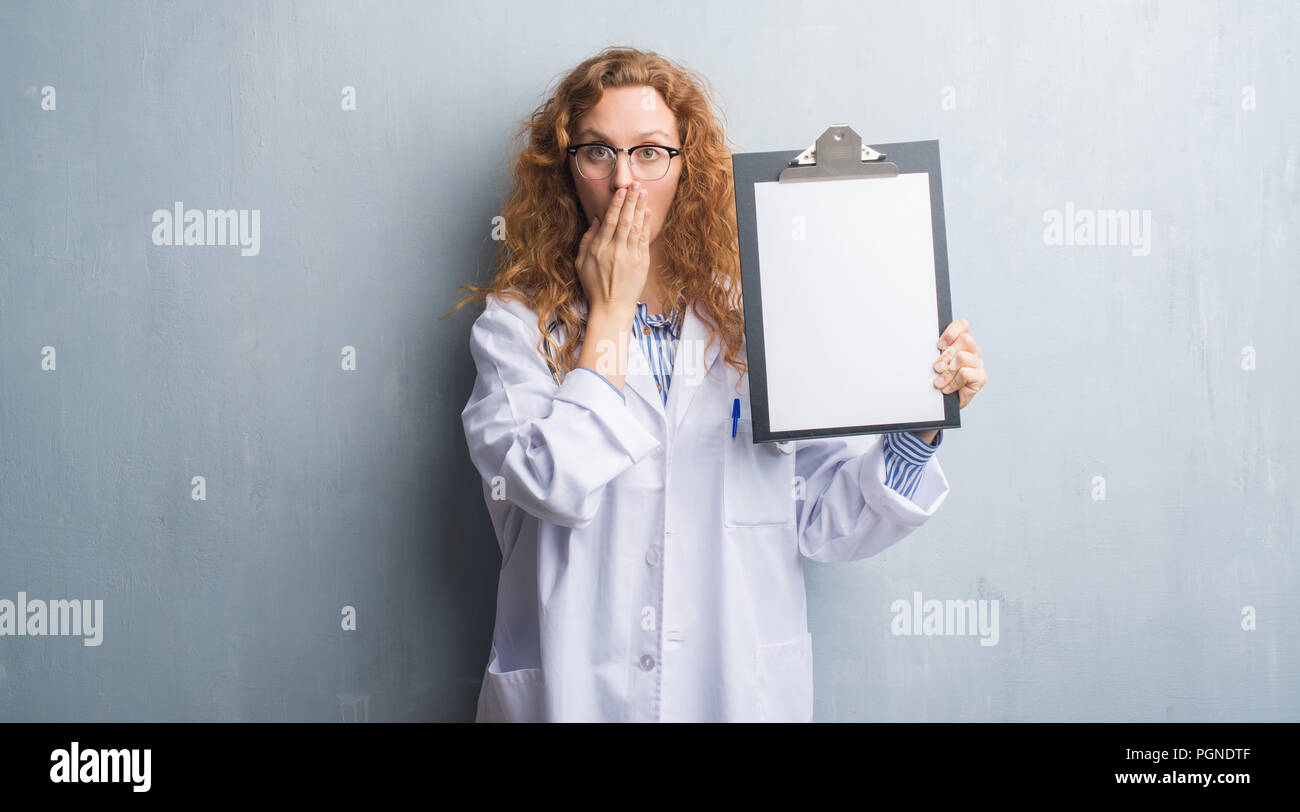 young redhead doctor woman over grey grunge wall showing clipboard