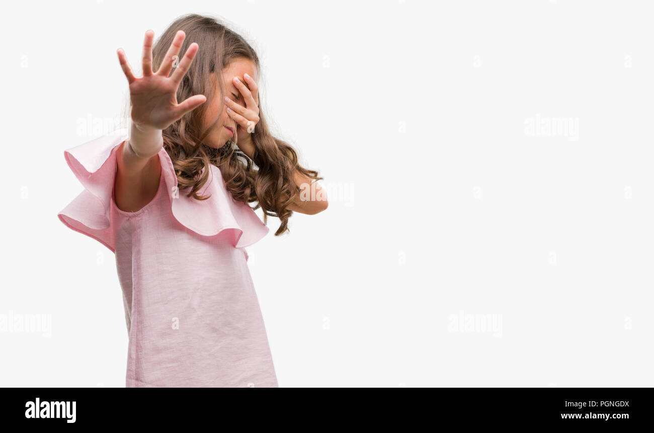 Brunette hispanic girl wearing pink dress covering eyes with hands and doing stop gesture with sad and fear expression. Embarrassed and negative conce Stock Photo