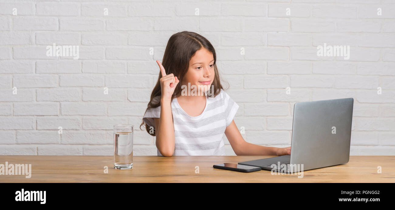 Young hispanic kid sitting on the table using computer laptop surprised ...