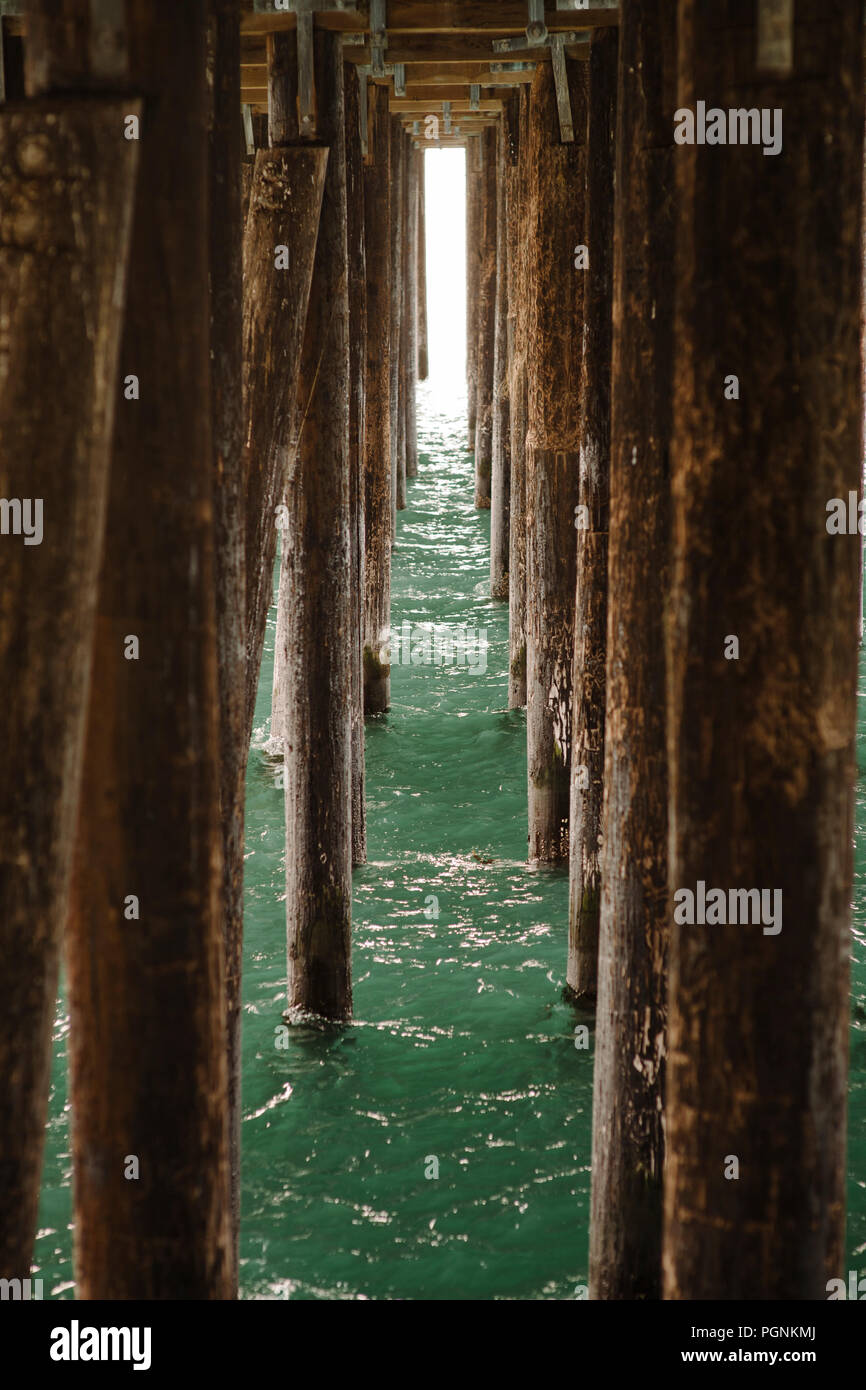 Light peers through wooden pylons under a pier Stock Photo