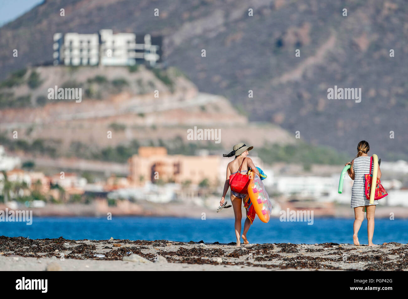 San Carlos, Sonora.  Turistas mujeres en bikini o traje de baño, caminan bajo el sol a la orilla de la playa, llevan con sigo sombrero para el sol y b Stock Photo