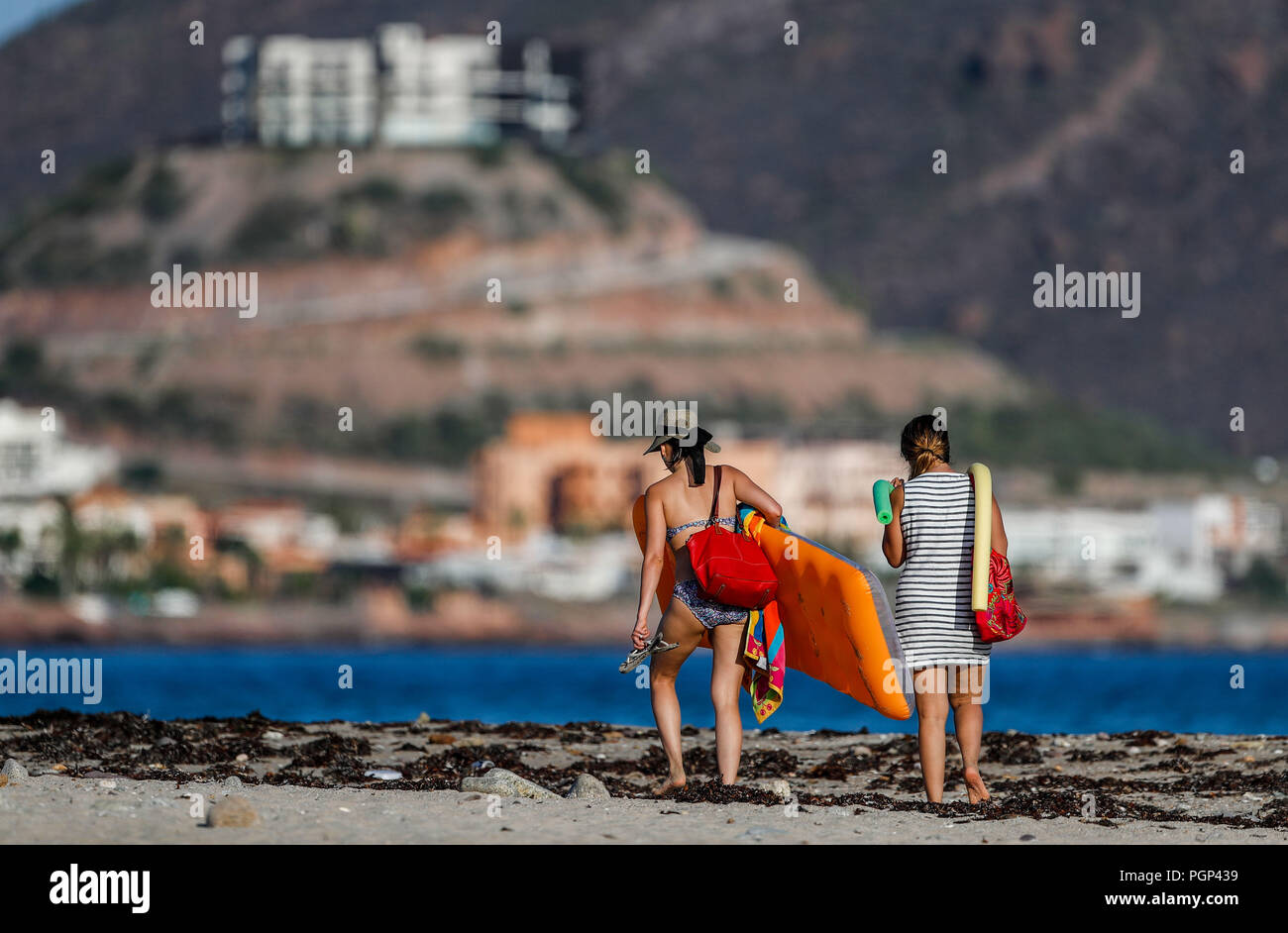 San Carlos, Sonora.  Turistas mujeres en bikini o traje de baño, caminan bajo el sol a la orilla de la playa, llevan con sigo sombrero para el sol y b Stock Photo